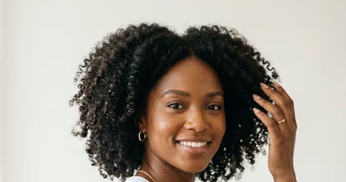 Smiling Black Woman with Curly Hair Touching Her Hair Against White Background
